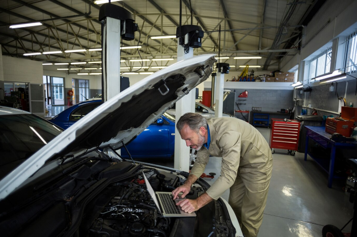 mechanic using laptop while servicing car engine