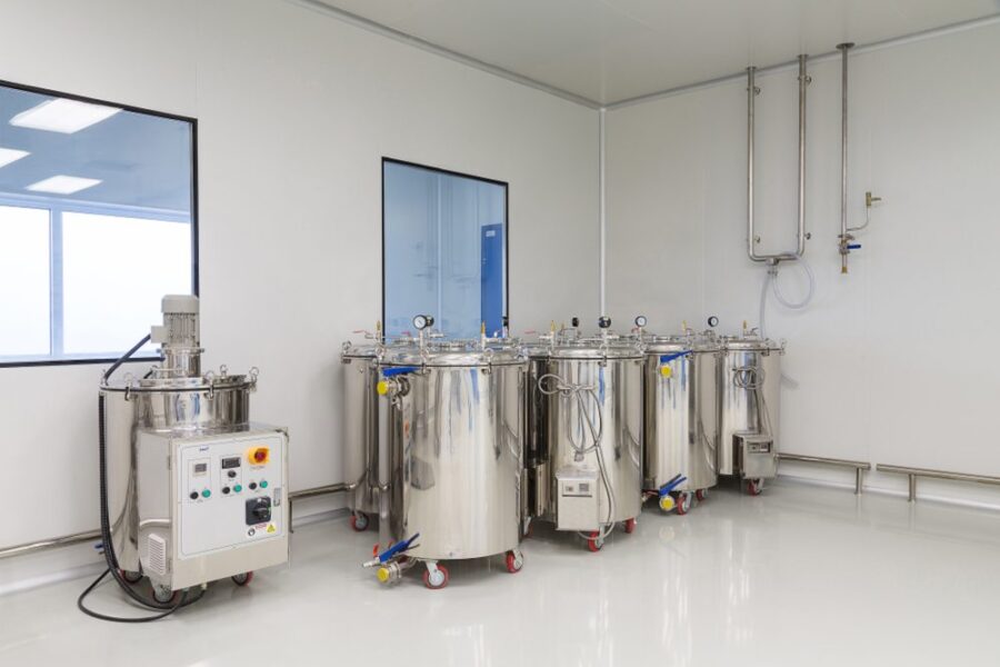 A clean, white room with four large stainless steel industrial tanks on wheels and a control panel, used for processing or storing liquids.